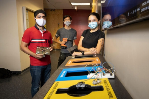 Three students stand in front of a waste sorting station with their sensor