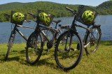 Three of the new bicycles purchased for the Active Transportation at Gault project are parked near a lake with green helmets in their baskets. 