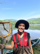 Smiling young woman in front of the lake at the Gault Nature reserve, wearing fishing gear.
