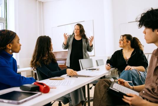 teacher in a classroom with students seated around a table