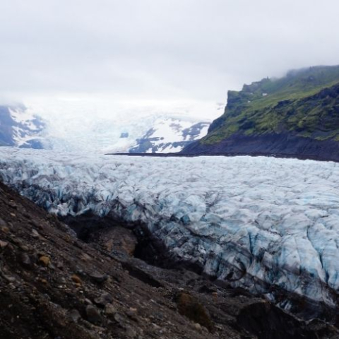 artic with ice sheet and unveiled dirt and green mountain in the backgroud