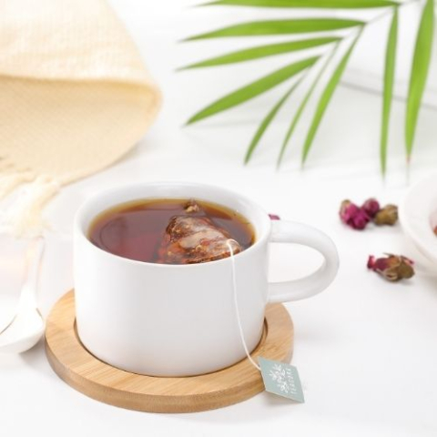 cup of tea with a teabag within it and a plant leaf on the side 