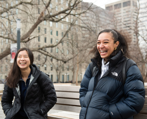 Two students with long hair smiling on cold day on campus