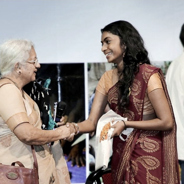 A student and elderly woman greeting each other, both wearing Indian saris.