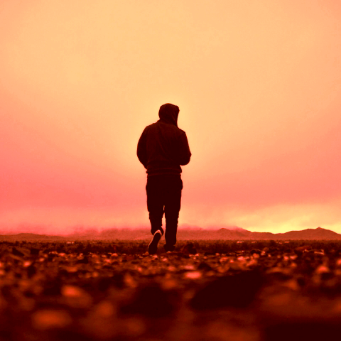 A person walking towards the horizon with a red background.