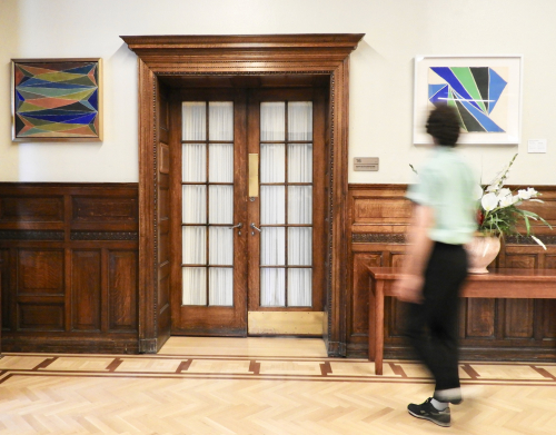 View of the paintings by Marian Scott in Old Chancellor Day Hall with a student walking by
