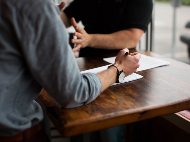 Image of two people interacting at a table with a pen and paper