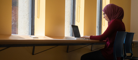 Student sitting in a passageway at a computer studying
