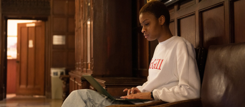 Student in a McGill sweatshirt sitting and reading a laptop
