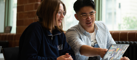 2 students sitting at a computer together, one is pointing at the screen