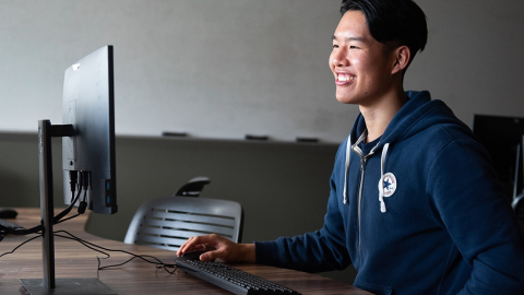 Student sitting at a desktop computer smiling