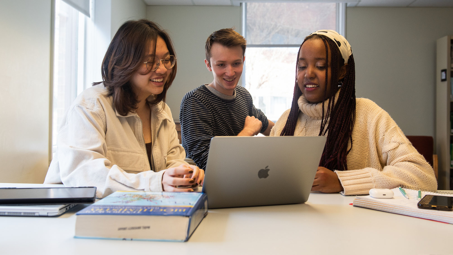 Three smiling McGill students gathered around a laptop.