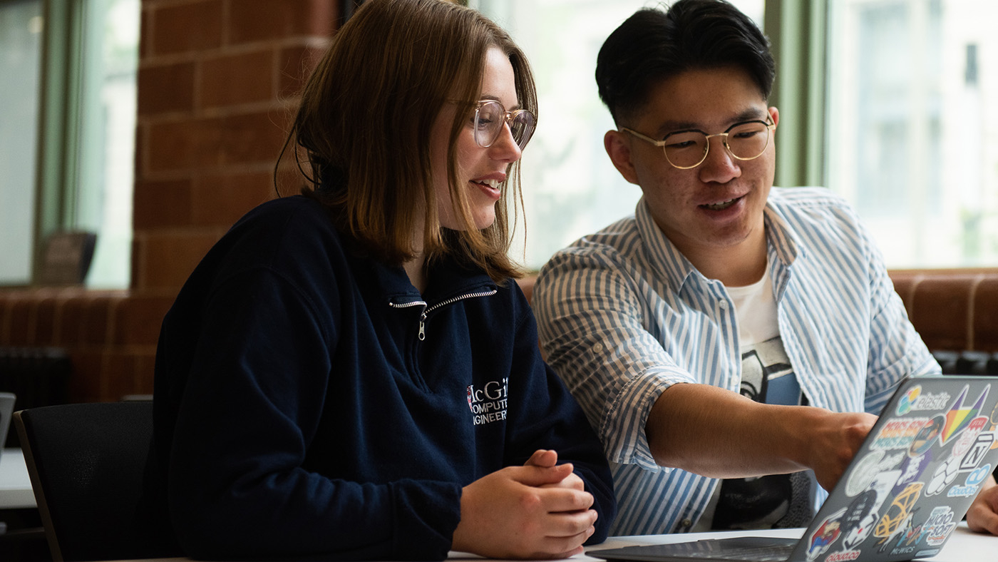 Two McGill students seated in front of a laptop having a friendly discussion about what they see on the screen