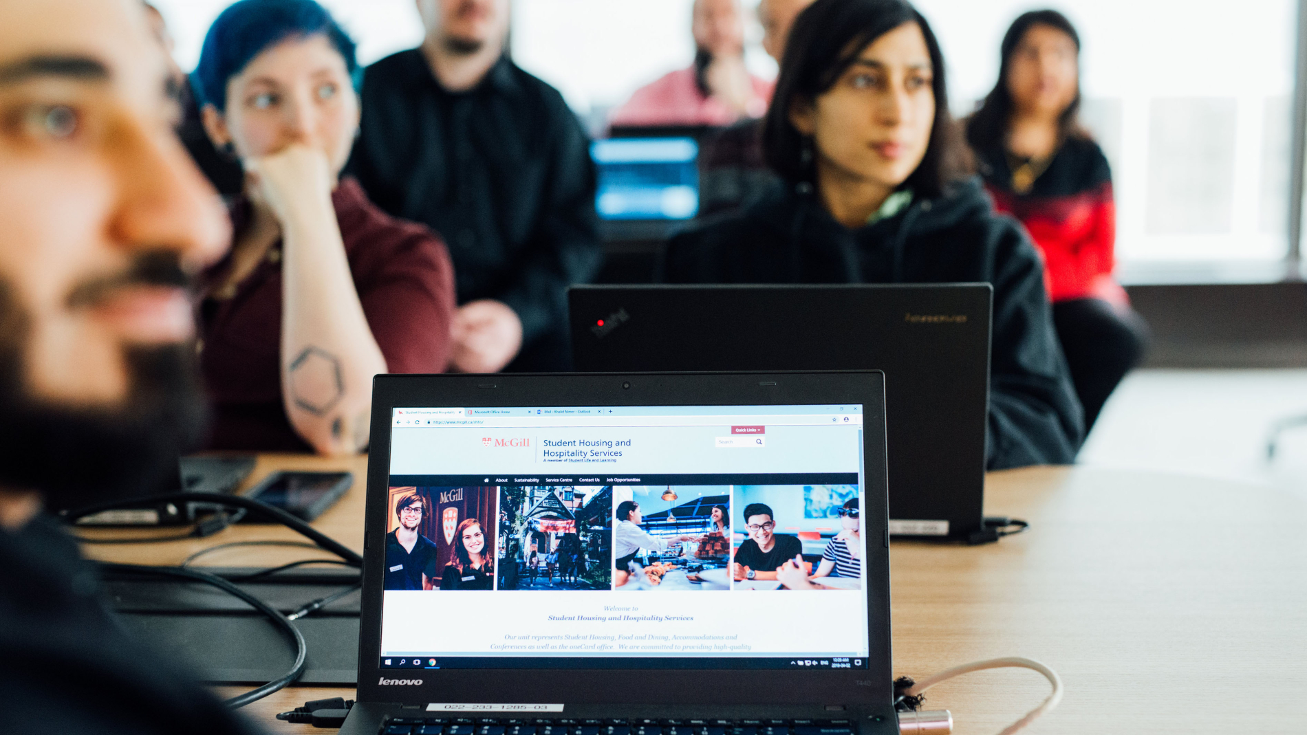 Students sitting at a desk in a classroom with a laptop screen in front of them, a McGill website is displayed on the screen.