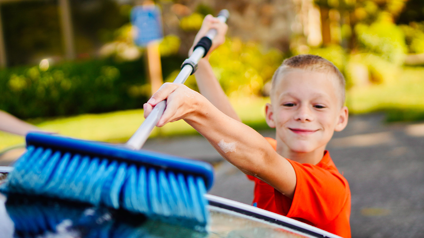 Young boy with a proud smile on his face cleaning a car with a scrub brush.