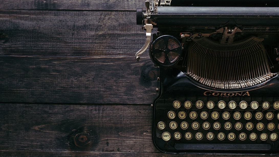 Old-timey typewriter sitting on a dark wood desk 