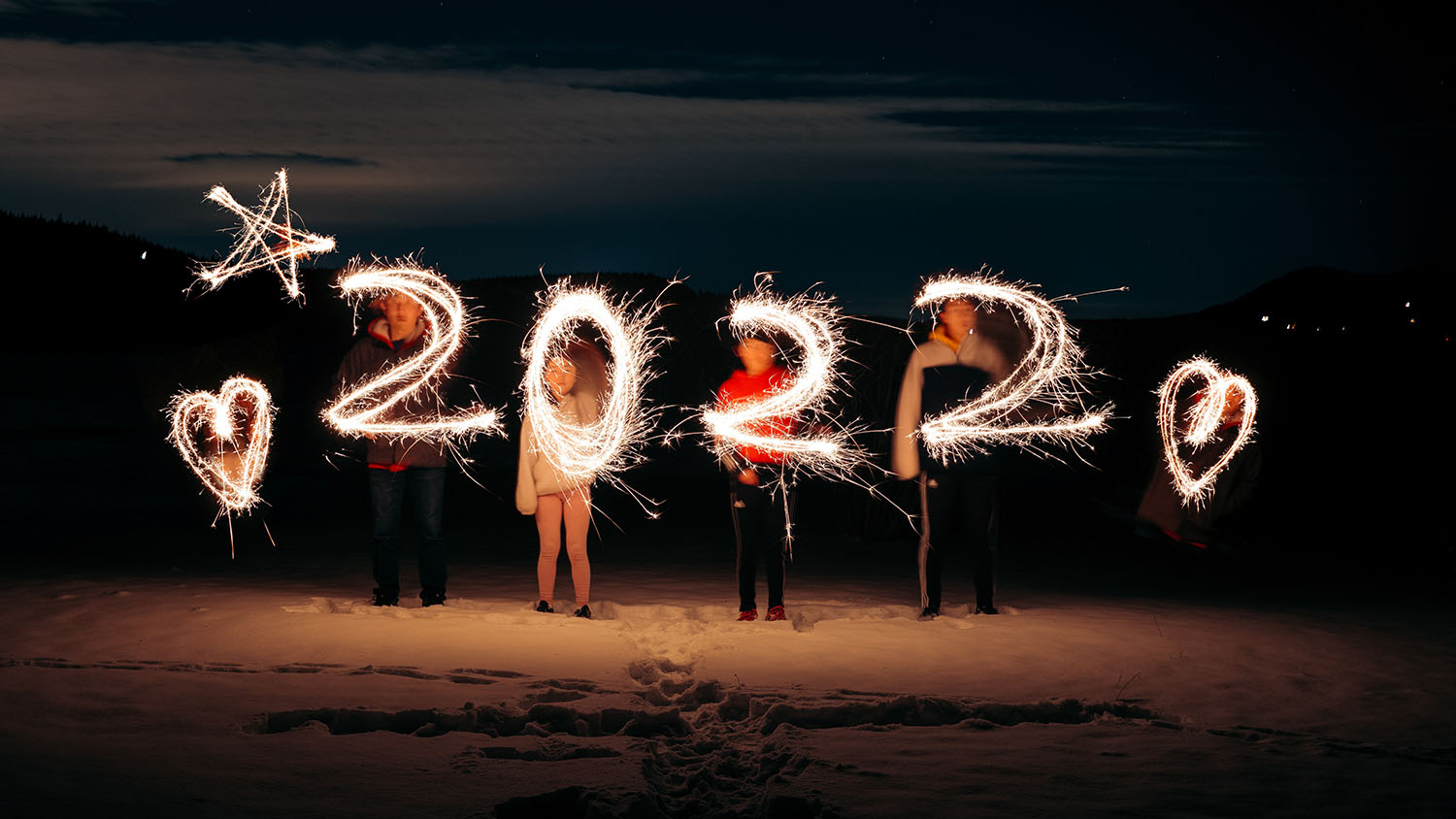 A lightpainting of the numbers 2022 created with sparklers by people standing on a beach.