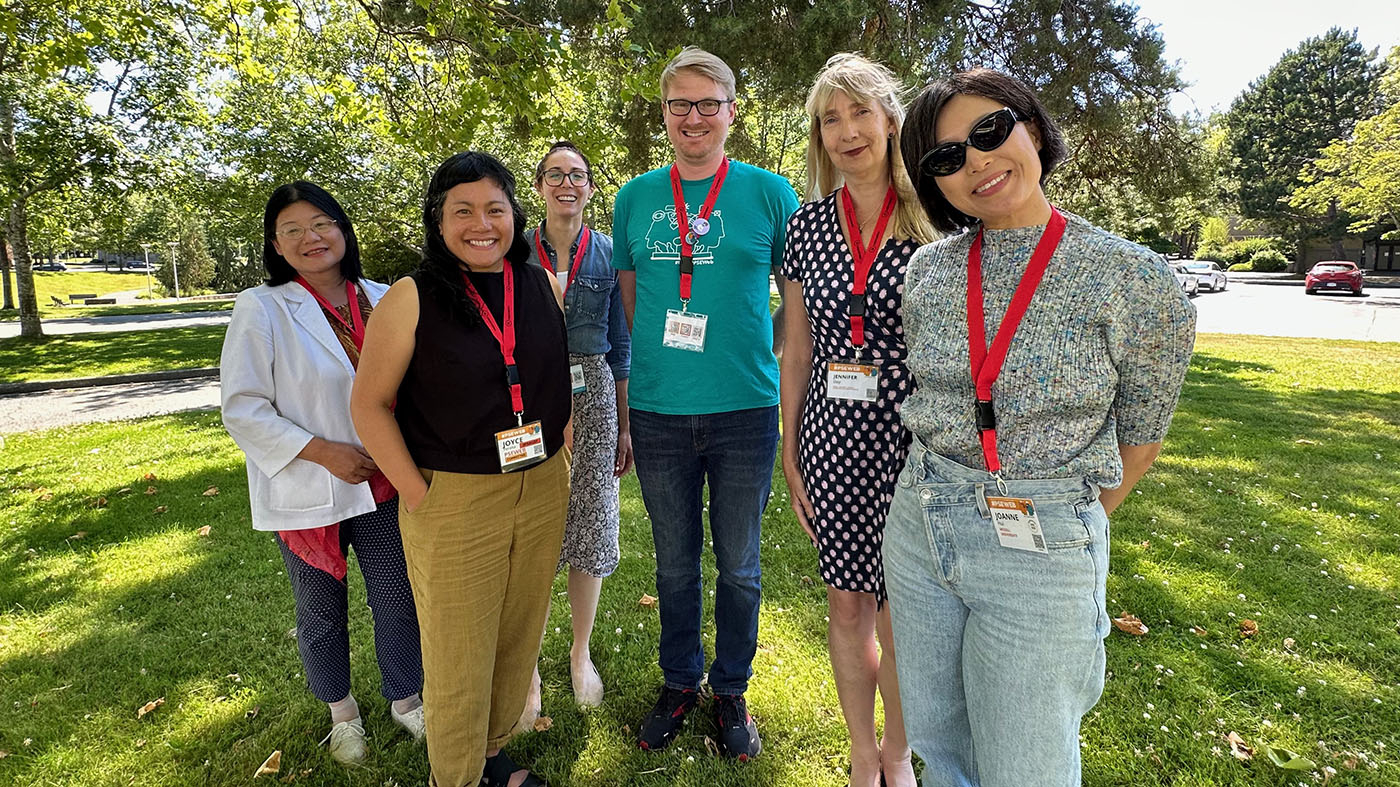 A group of McGill staff members at #PSEWeb 2023 standing on a lawn outside Cheko'nien House on UVic's beautiful campus.