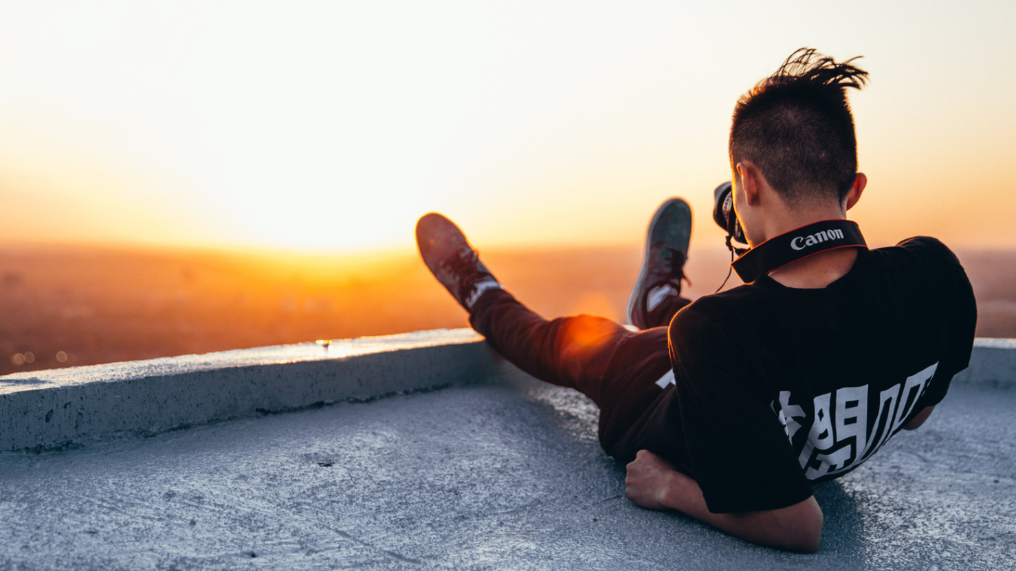 Photographer sitting outside on a rooftop capturing the distant sunset