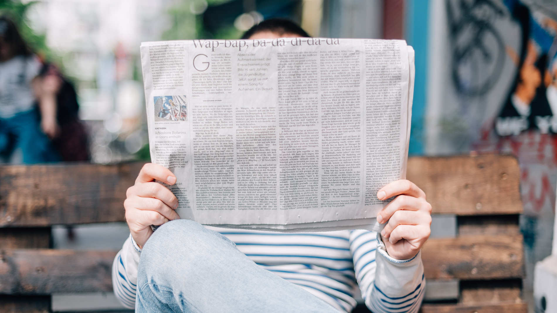 Man sitting outside on bench reading newspaper