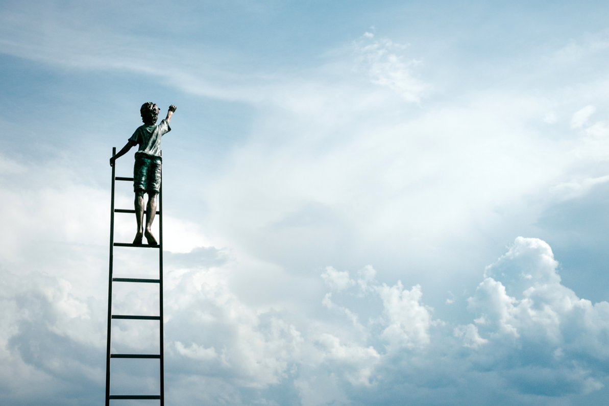 boy on ladder reaching to clouds in sky